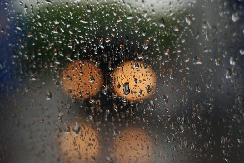 rain drops falling down on three yellow lightbulbs in front of a window