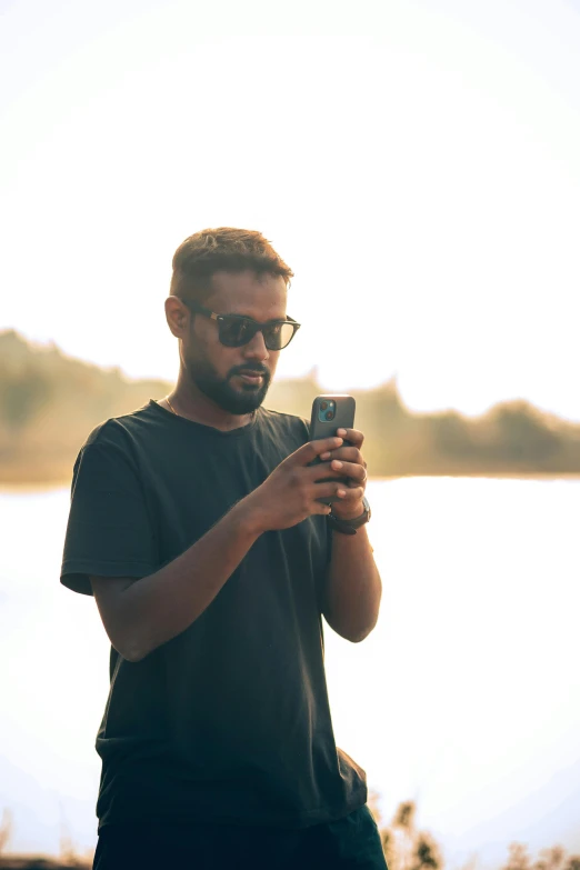 a man with sunglasses and dark t - shirt uses his cell phone