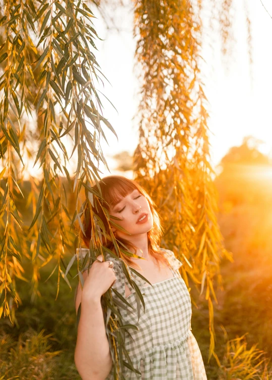 a woman in a green dress stands beneath a willow tree