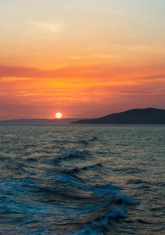 the sun setting over a body of water with a island behind it