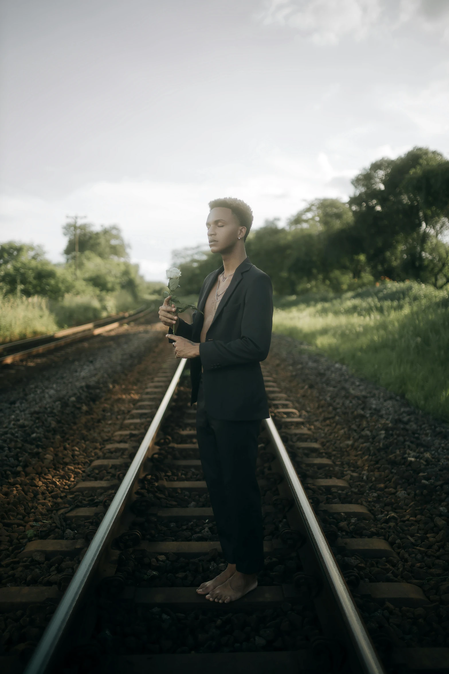 a man in suit and tie stands on a railroad track