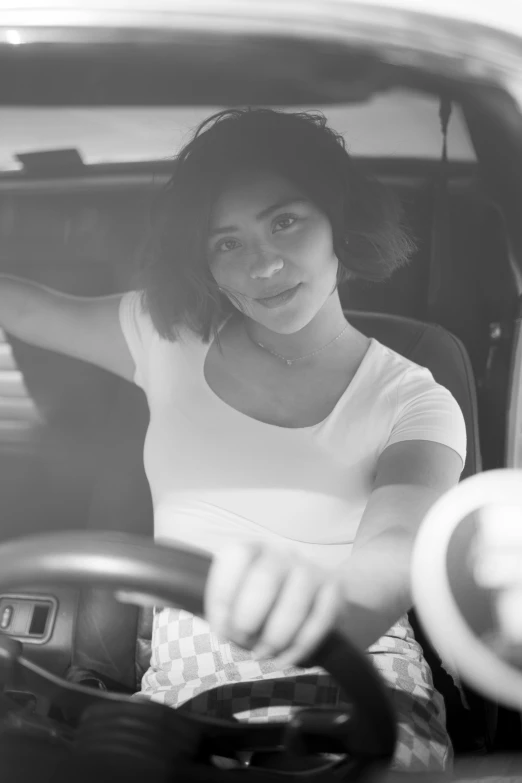 a woman in a car smiling with steering wheel out