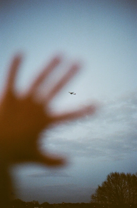 an airplane flies by behind a blurred hand