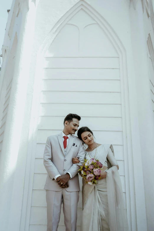 two people in white attire posing next to a tall church