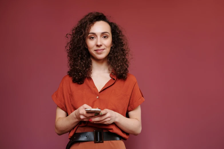 woman standing in front of a maroon background and looking at a cell phone