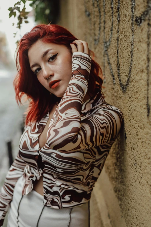 a woman with red hair leaning against a wall and looking at the camera