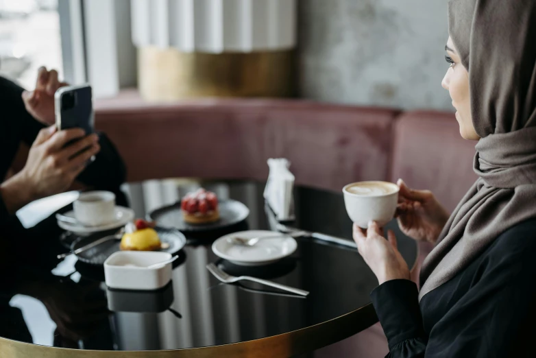 two people are at a table in a cafe, looking at a phone