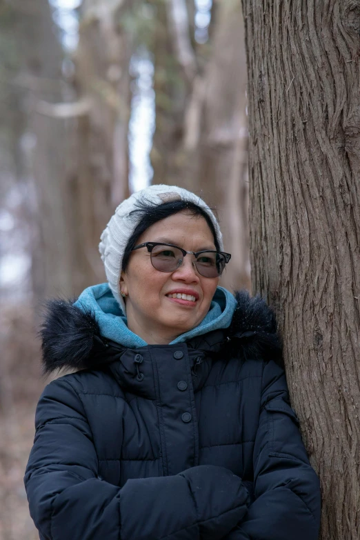 woman wearing glasses standing behind a tree in the woods