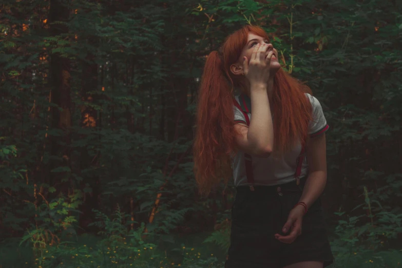 there is a young woman with long red hair walking and looking up in the forest