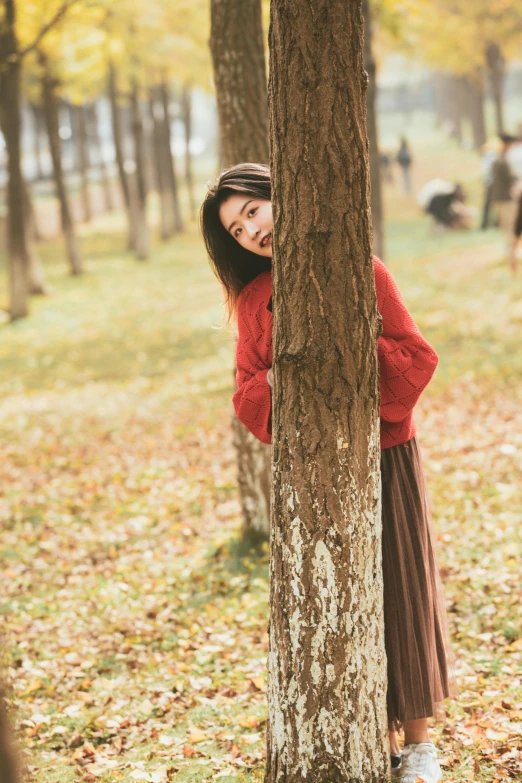 a girl standing behind a tree in a park