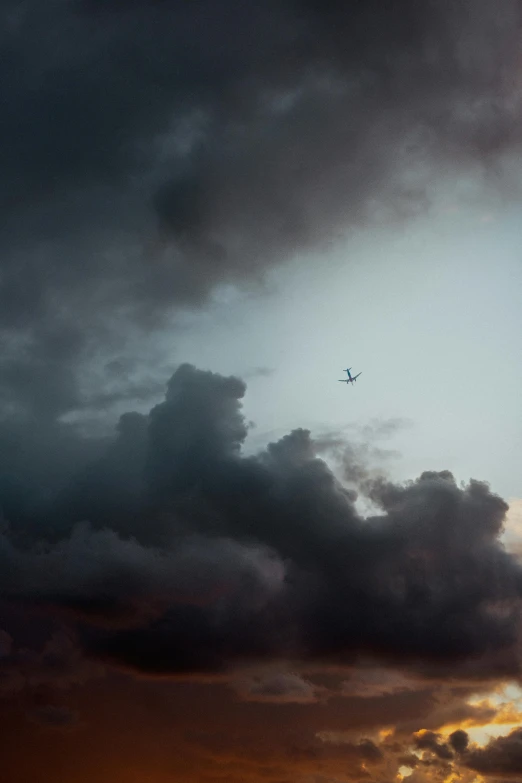 an airplane flies through the clouds in an orange and grey sky