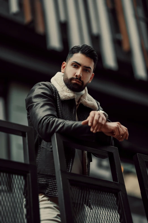 a bearded man with his hands crossed leaning on a rail