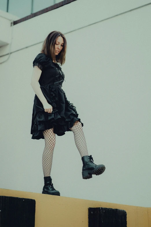 a girl in a dress and boots standing on the edge of a wall