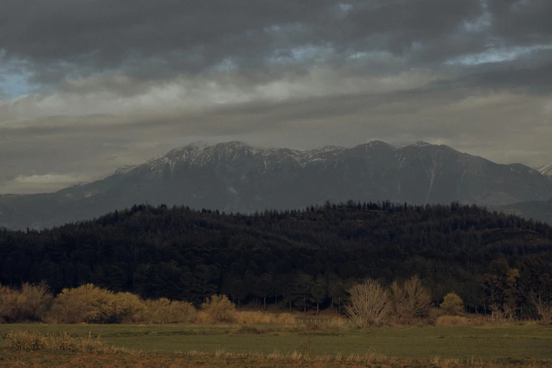 the mountains and trees are behind the cloudy sky