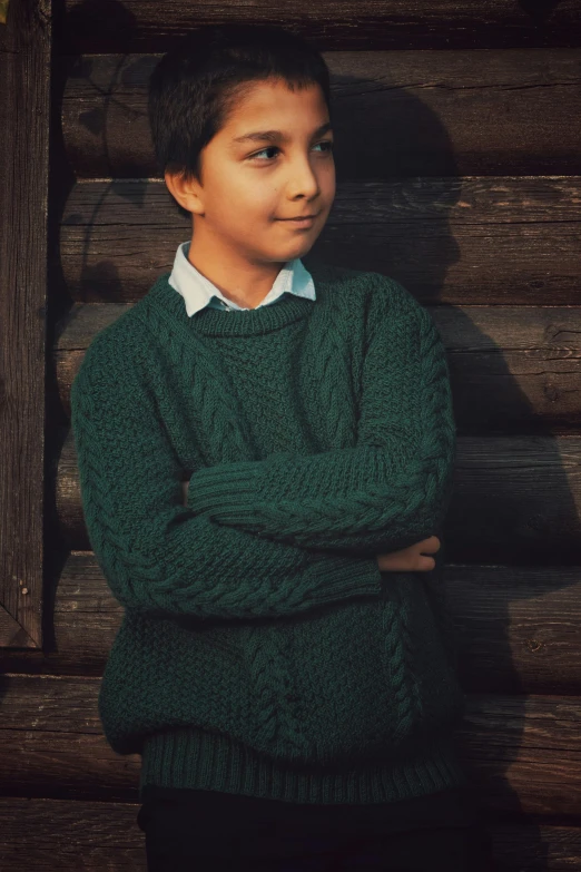 a  in green sweater standing against wooden wall