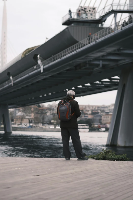 a person standing near the water near a bridge