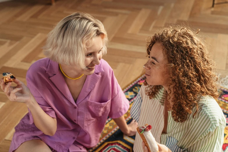 two women sit on the floor, one holding a phone