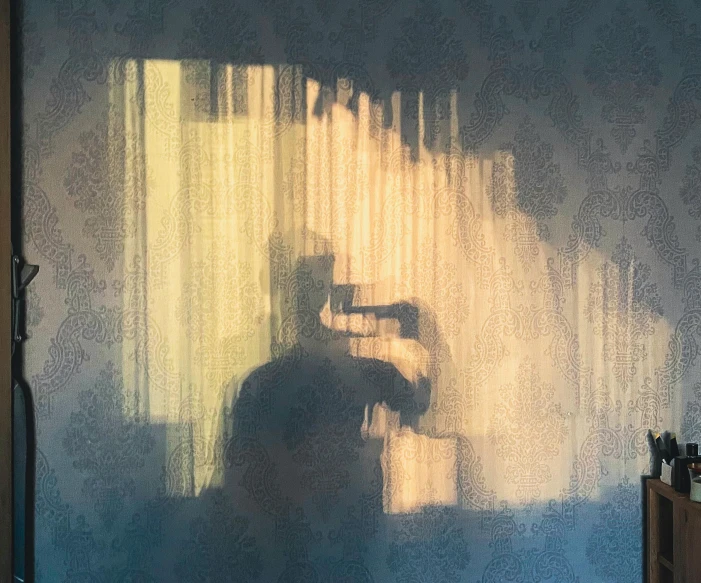 someone standing in front of a wall with sunlight streaming through the curtained windows