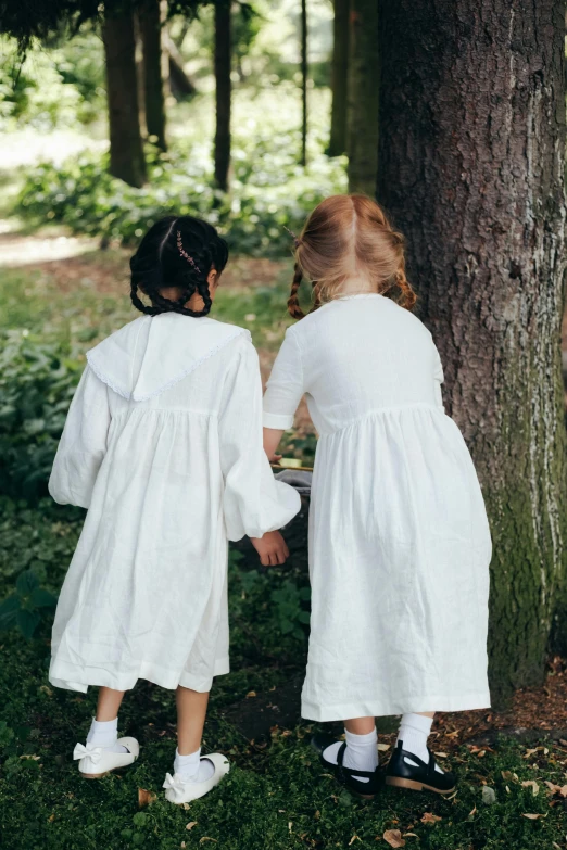 two small children in white dresses are standing in the woods