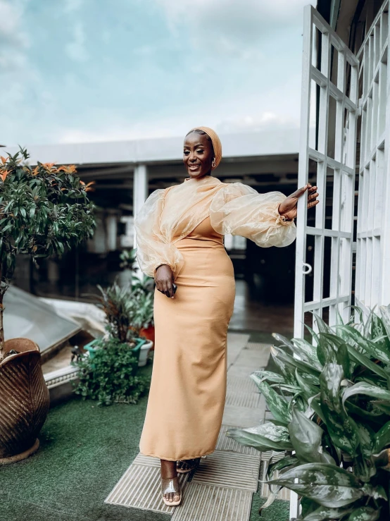 an african woman dressed in beige, posing with open arms and legs