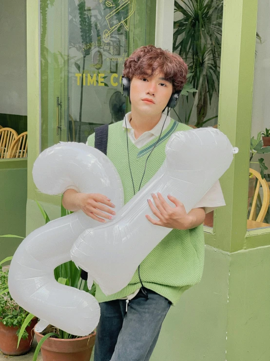 a boy in a green shirt holding some white balloons