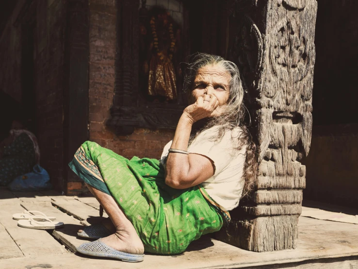 old woman sitting on the ground in front of a tree