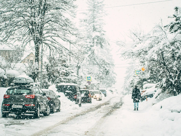 a man walking along a snow - filled street with cars
