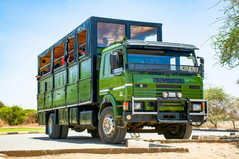 a large green truck on the road with trees in the background