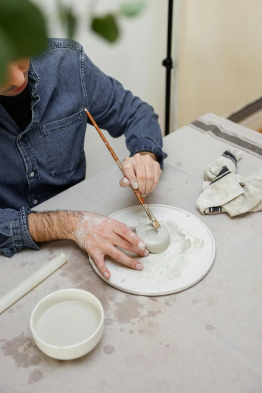 an artisan painting on an oval shaped object with white paint