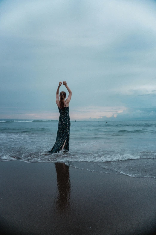 a woman in black dress dancing on beach with cloudy sky