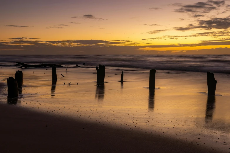 a sandy beach with a wooden pier sticking out of the water