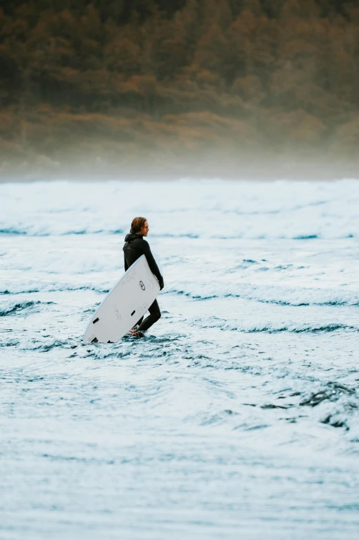 a woman walking across a body of water holding a white surfboard