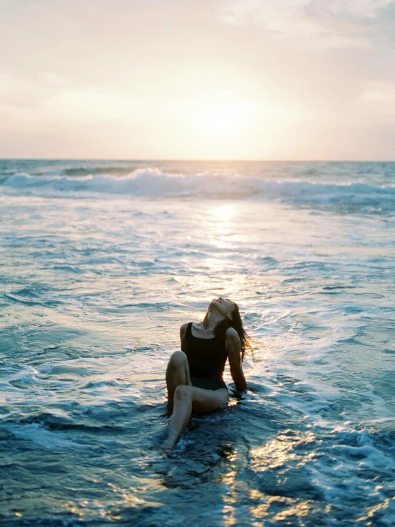 woman in bathing suit sitting on surfboard in the ocean