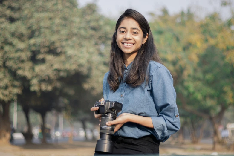 a beautiful woman holding a camera by trees