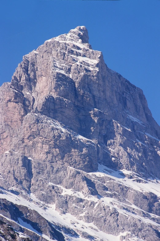 a mountain with a snow covered top and many patches of green in the foreground