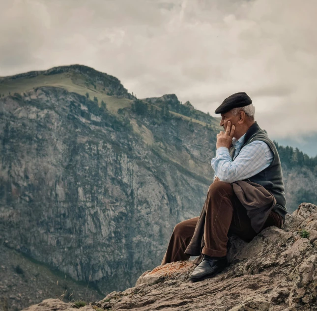 an old man sits on a cliff with a phone