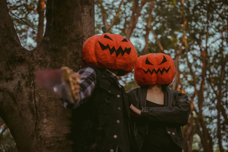 two people wearing pumpkin hats in a forest