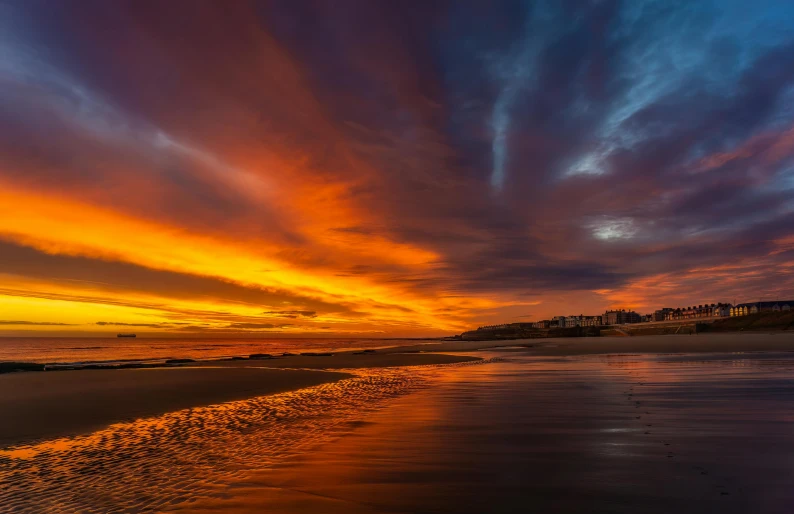 a beach with orange and blue clouds at sunset