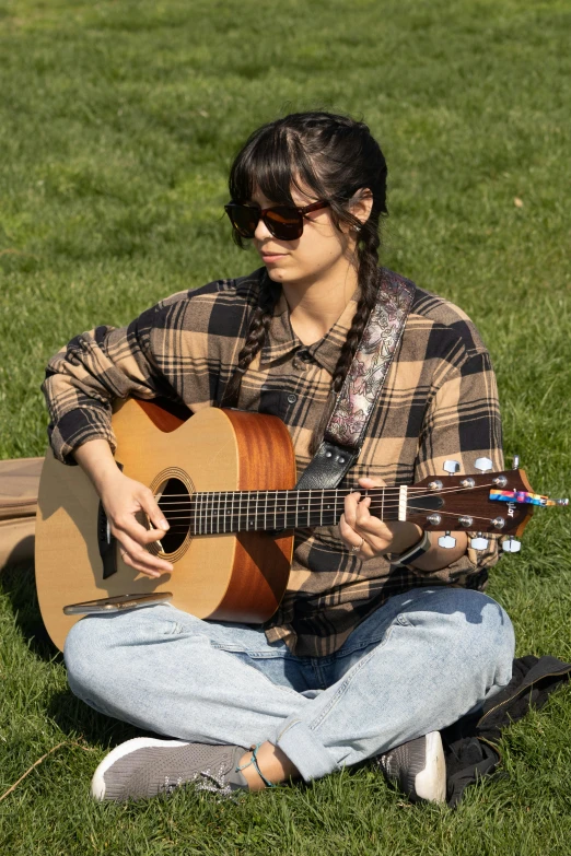 woman sitting on the ground playing guitar on a field