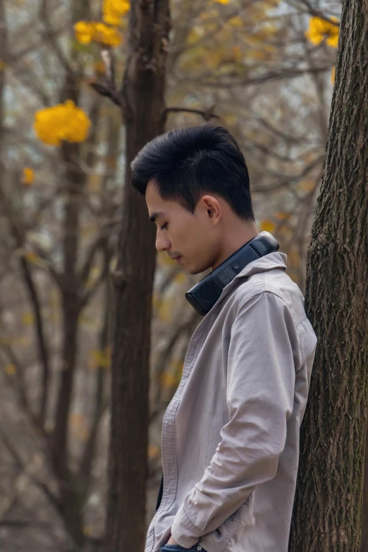 a young asian man leaning on a tree