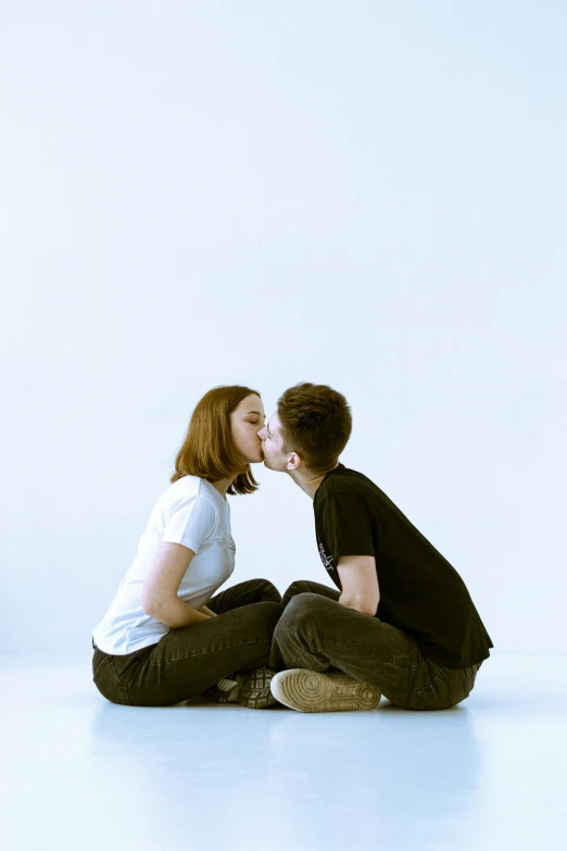a young couple sit on the floor in front of a white wall