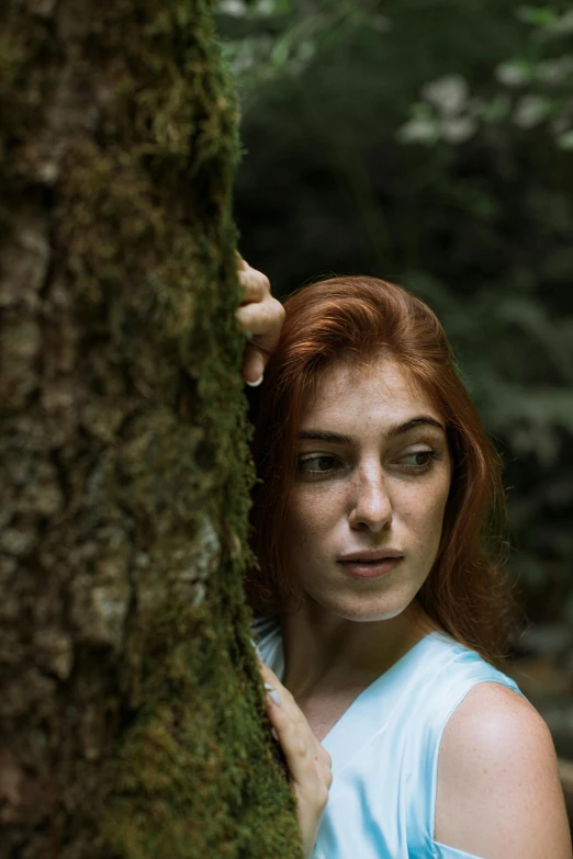 a woman standing next to a tree in a forest