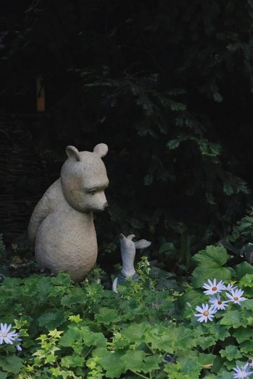 a statue of a bear and her cub sitting on a meadow full of daisies