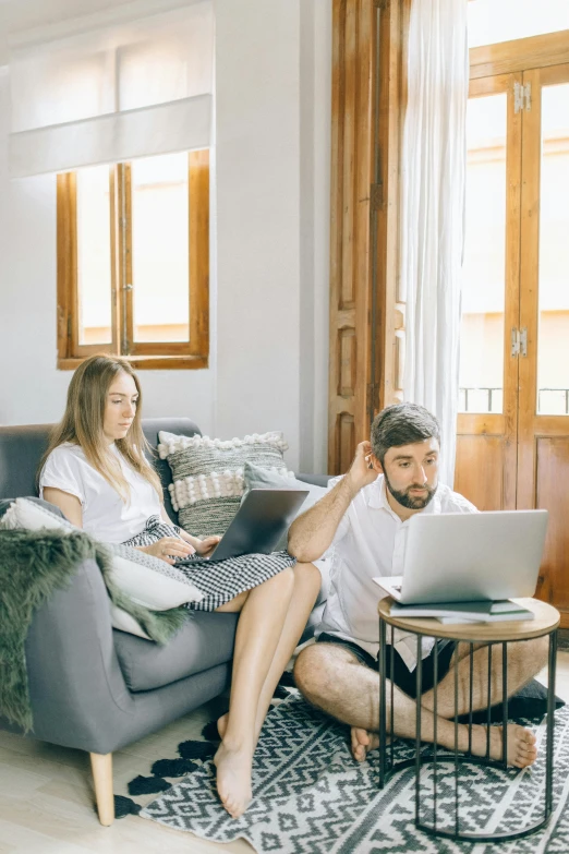 a couple sits on a couch, looking at soing on a laptop