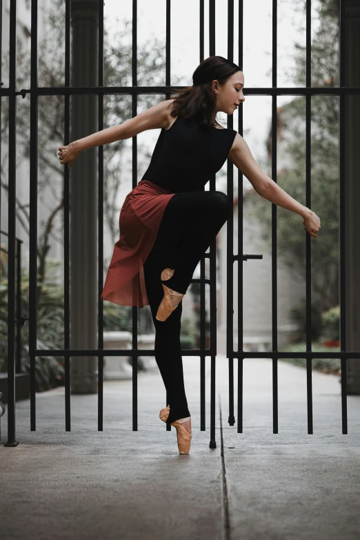 a ballerina leans on the fence to do ballet