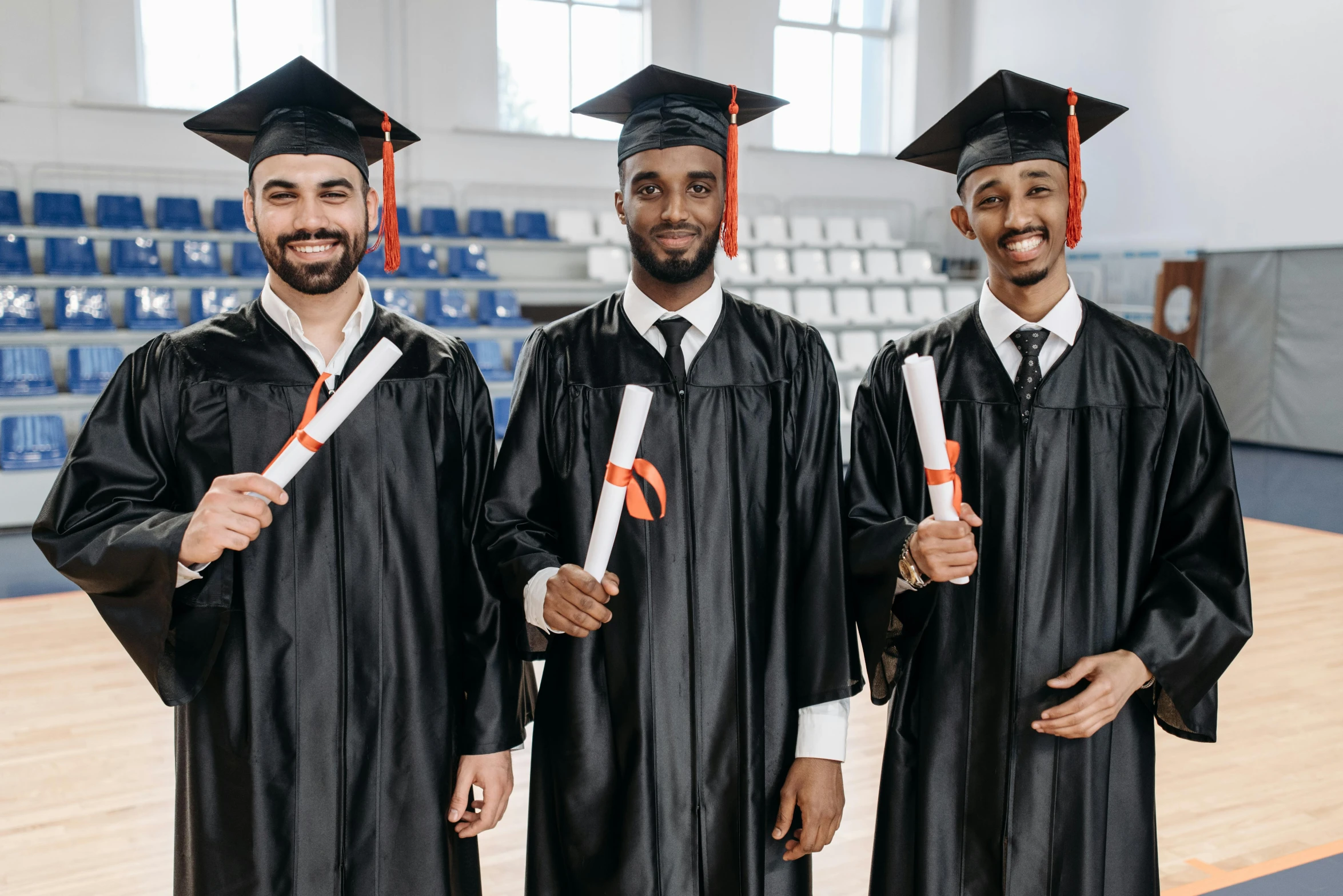 three young men are in graduation robes holding orange and white paper scissors