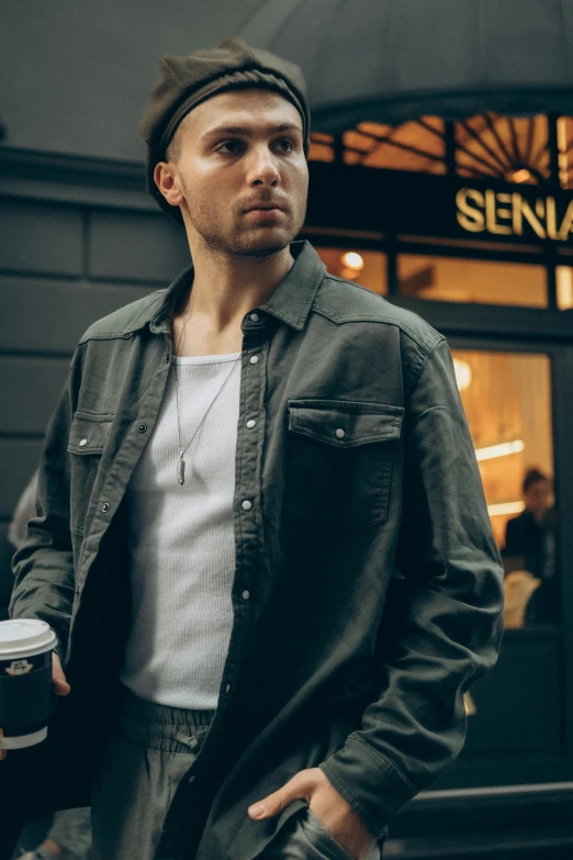 a young man in a grey denim jacket and hat holds a coffee mug