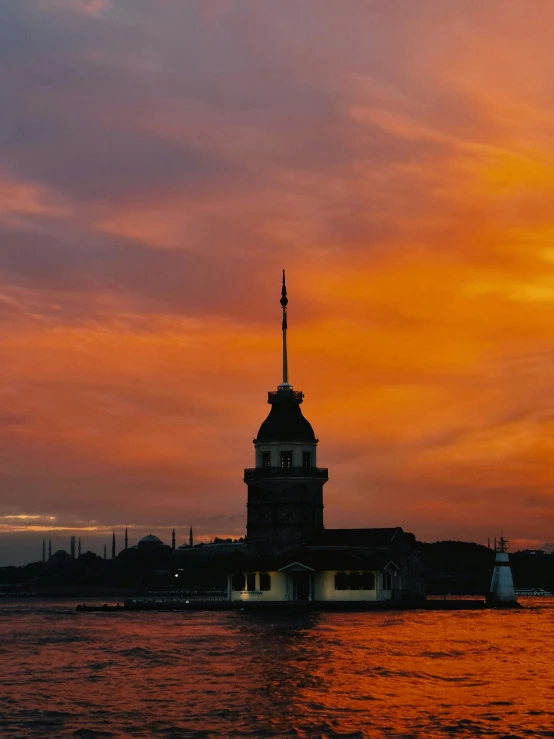 a water tower rises above the water in an orange sky