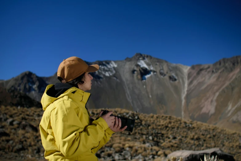 a man with a yellow jacket standing near a mountainside