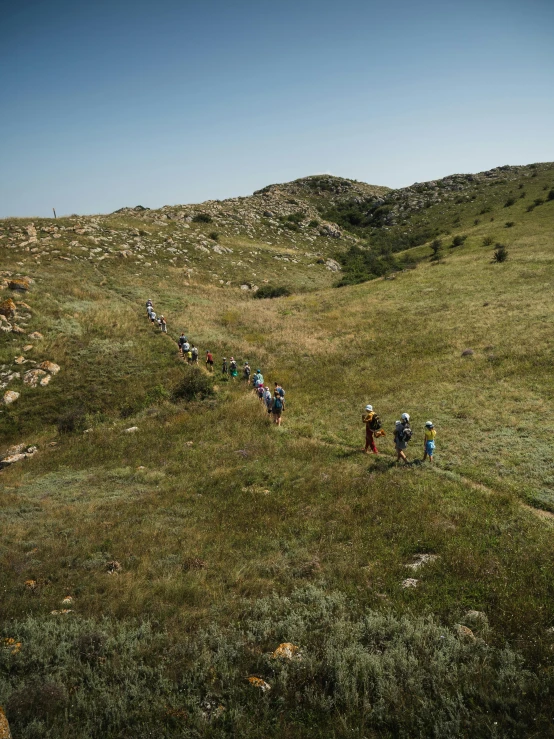 a group of people hiking up a grass covered hill